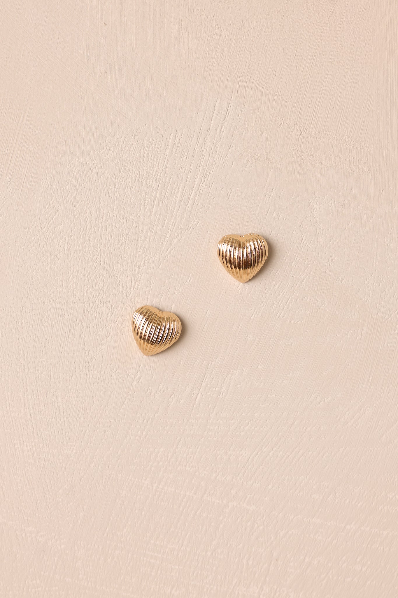 A close-up view of the small gold heart stud earrings with textured gold detailing and secure back posting, shown from the front.