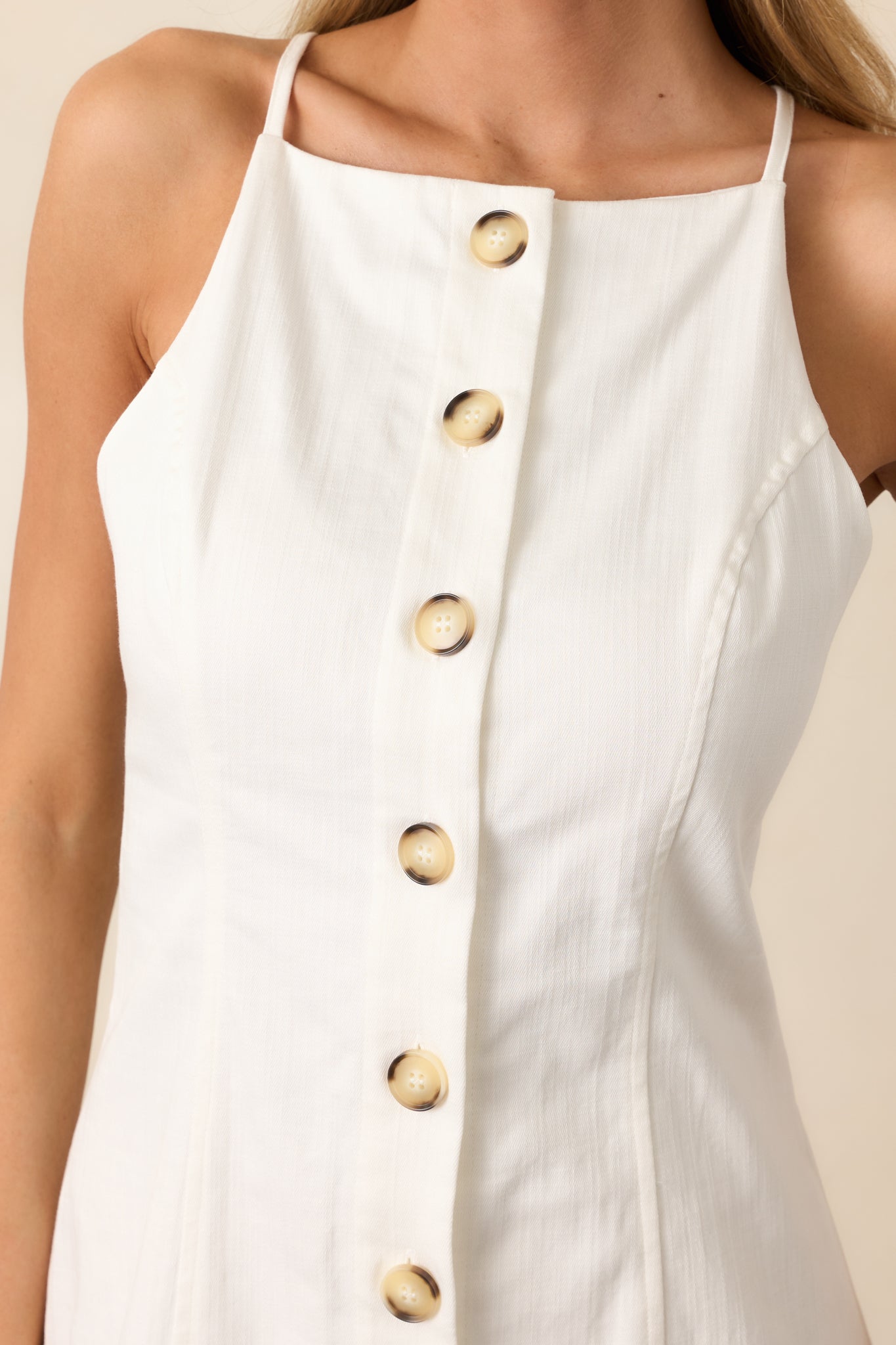 A front view of the ivory mini dress showcasing the halter neckline, button front design with tortoise buttons, and sleeveless cut.