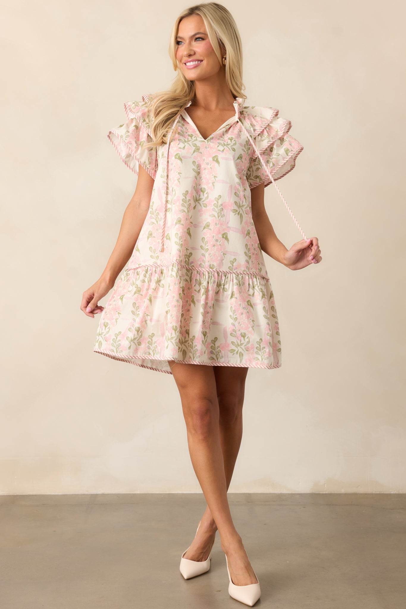 Full body view of a pink mini dress featuring a ruffle neckline, relaxed fit, and flutter sleeves, showcasing the delicate floral design.