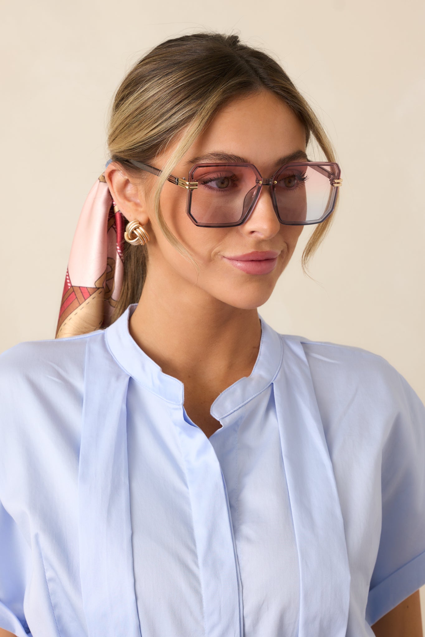 A bold pair of sunglasses with a pink-to-blue ombre square frame, sleek gold accents on the sides, and matching tinted lenses.