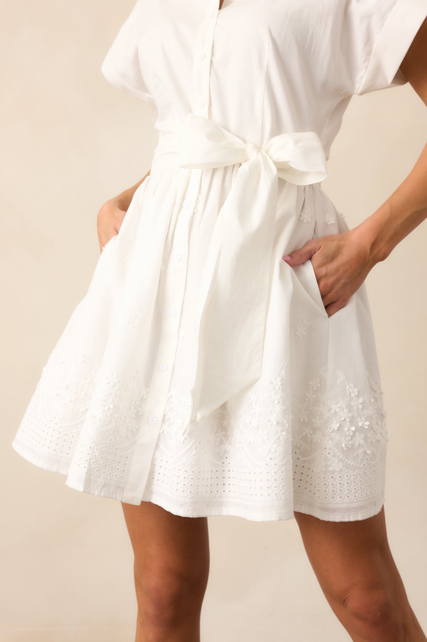 A detailed look at the embroidered hem of the white dress, showcasing the intricate stitching and the button front design, with the self-tie waistband adding a flattering structure.