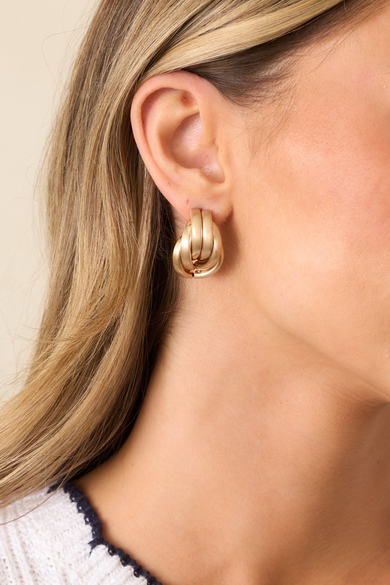 A close-up view of the gold earrings, highlighting their unique hoop design and matte gold finish.