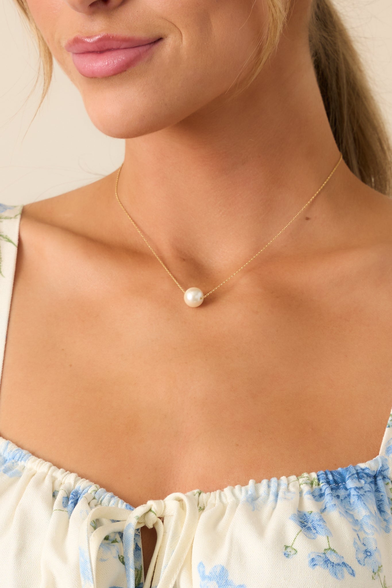 A very thin gold chain with a delicate ivory faux pearl pendant and a lobster claw closure, combining a classic look with secure fastening.