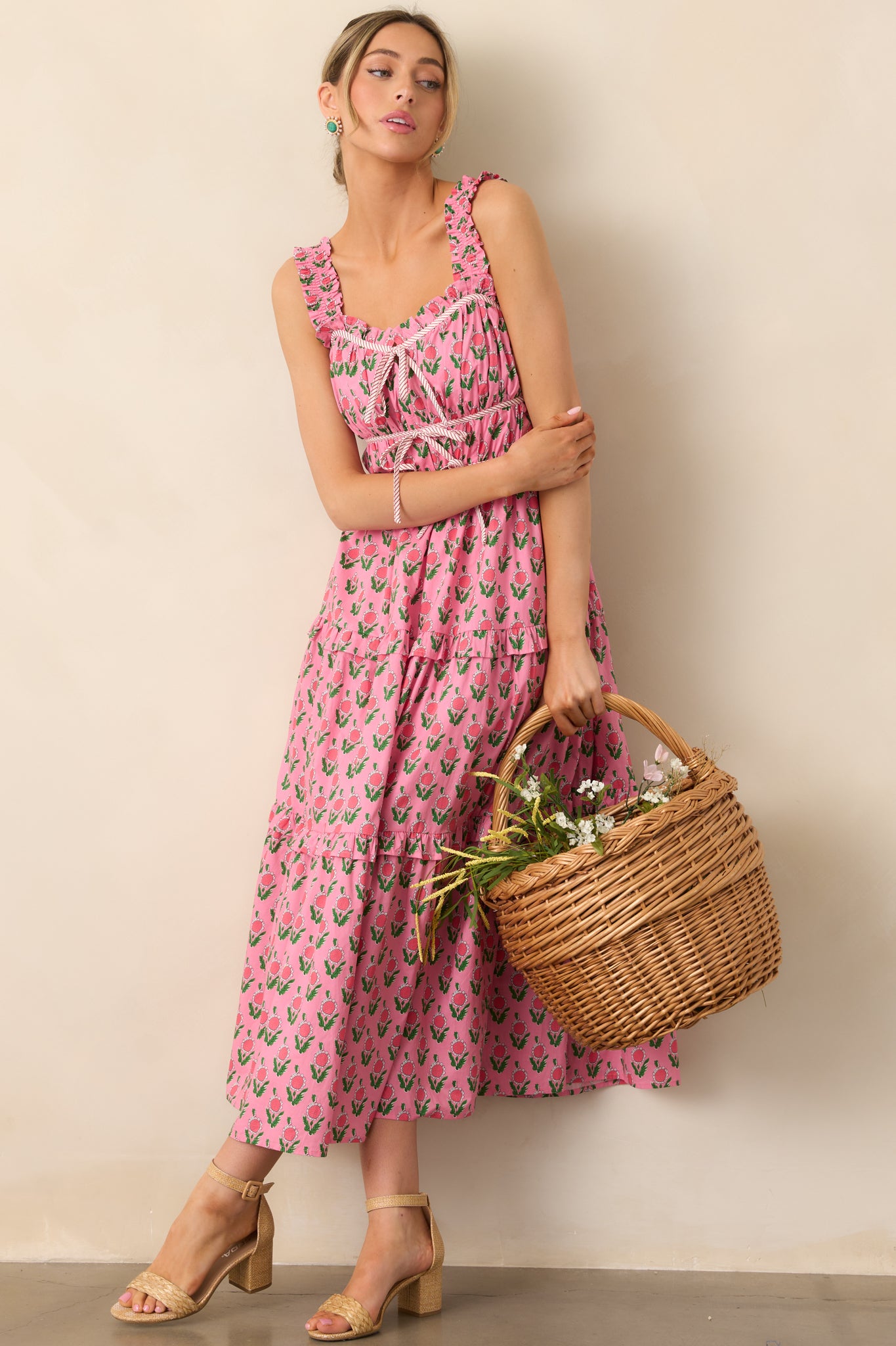 This pink dress features a three-tiered empire waist with bow tie detailing at the waist, along with flowing ruffle tiers below, creating a fun and feminine silhouette.