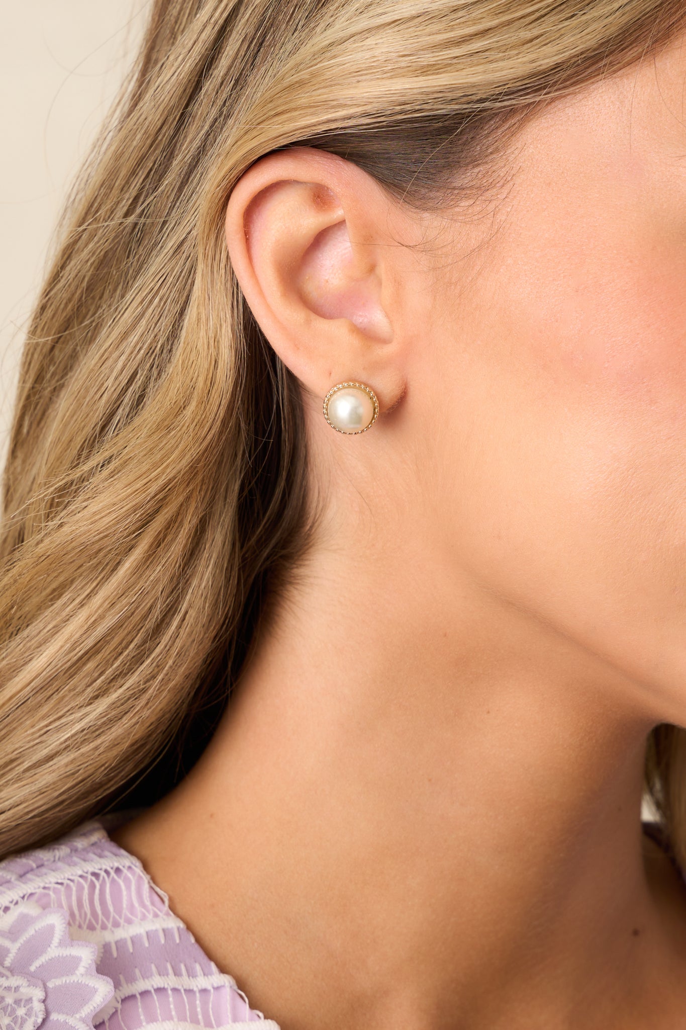 A pair of ivory pearl earrings with a stud design, featuring a large faux pearl encased in a braided gold border.