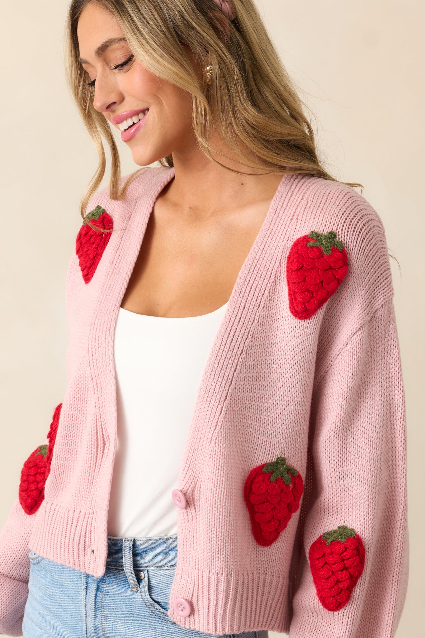 The pink cardigan from a slightly angled side view, showcasing the placement of the strawberry graphics and the long sleeves.