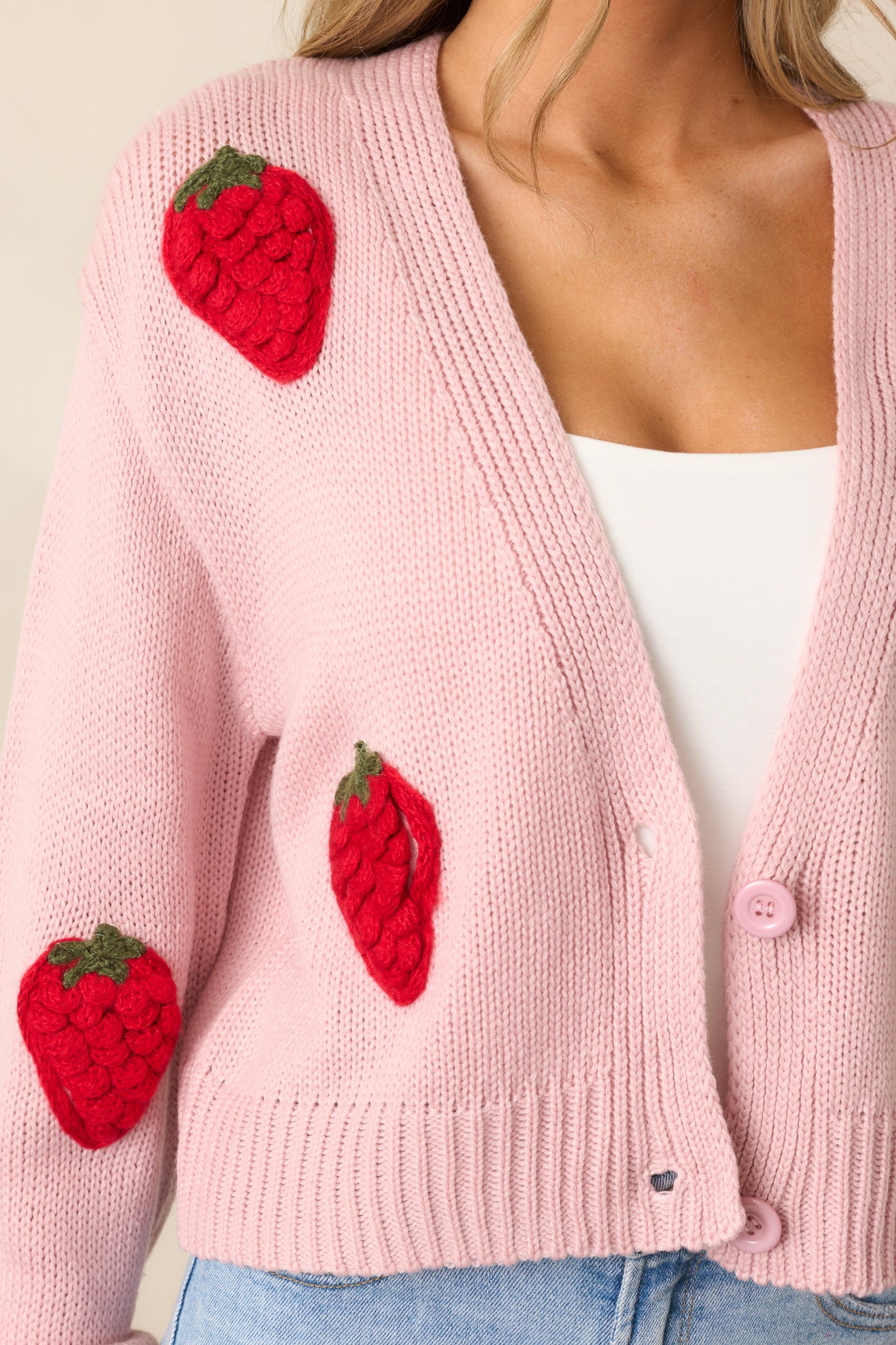 An extreme close-up of a strawberry graphic on the cardigan, highlighting the vibrant color and detailed stitching.