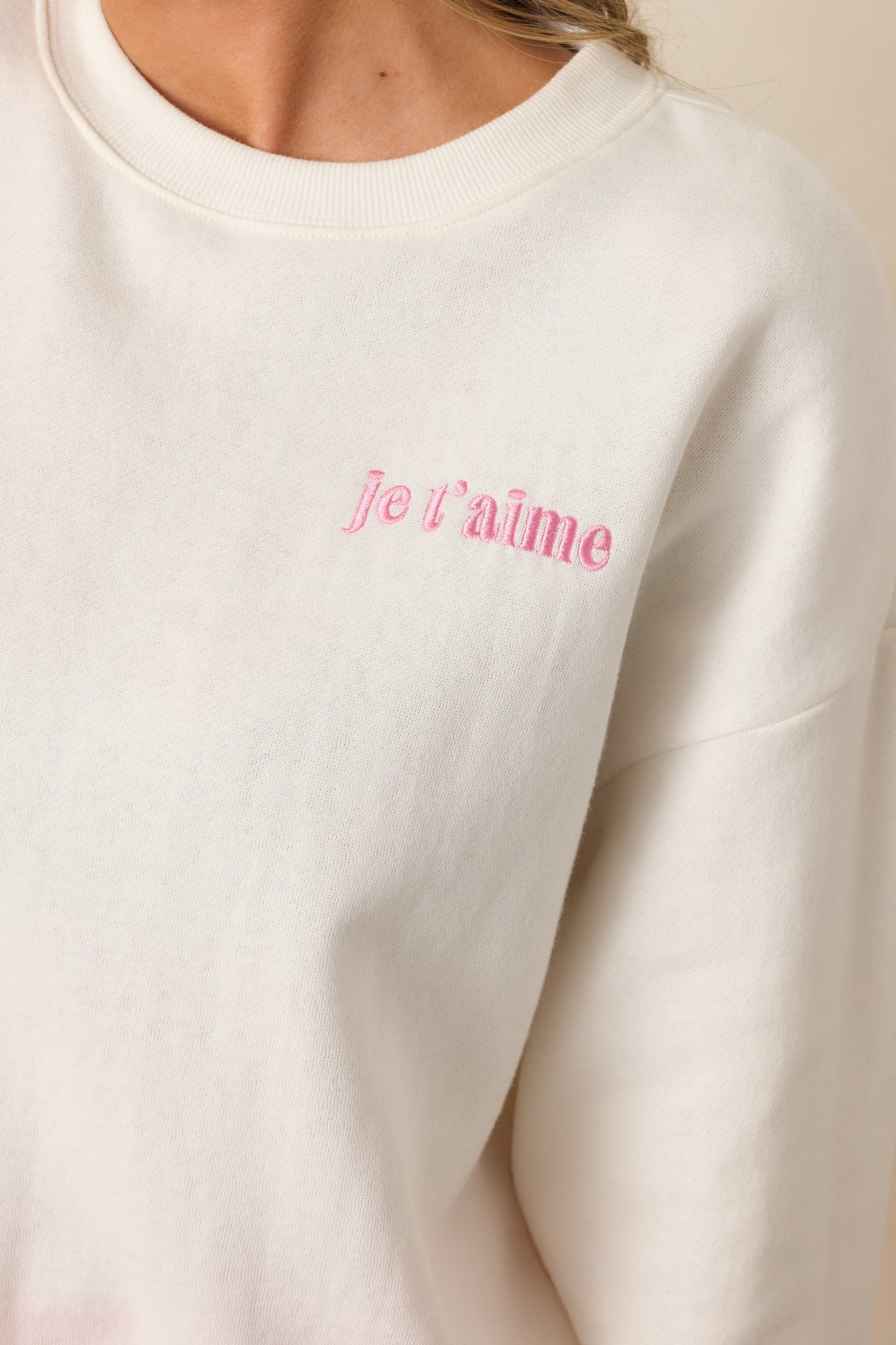 A close-up image focusing on the "je t’aime" embroidery on the chest of the ivory sweatshirt, showcasing the intricate stitching and the soft fabric texture.