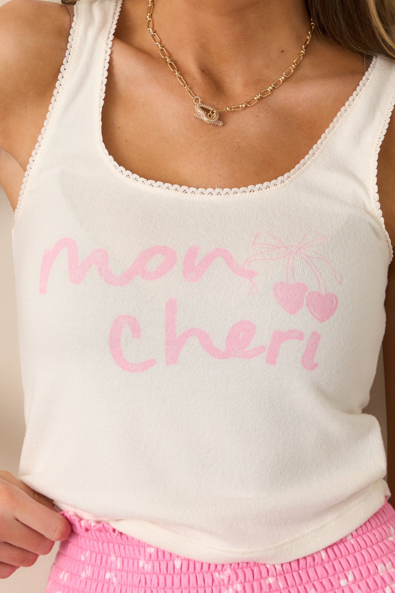 A close-up of the scoop neckline and lace trim, capturing the intricate lace detailing and the smooth fabric of the ivory tank top with the "Mon Chéri" graphic.