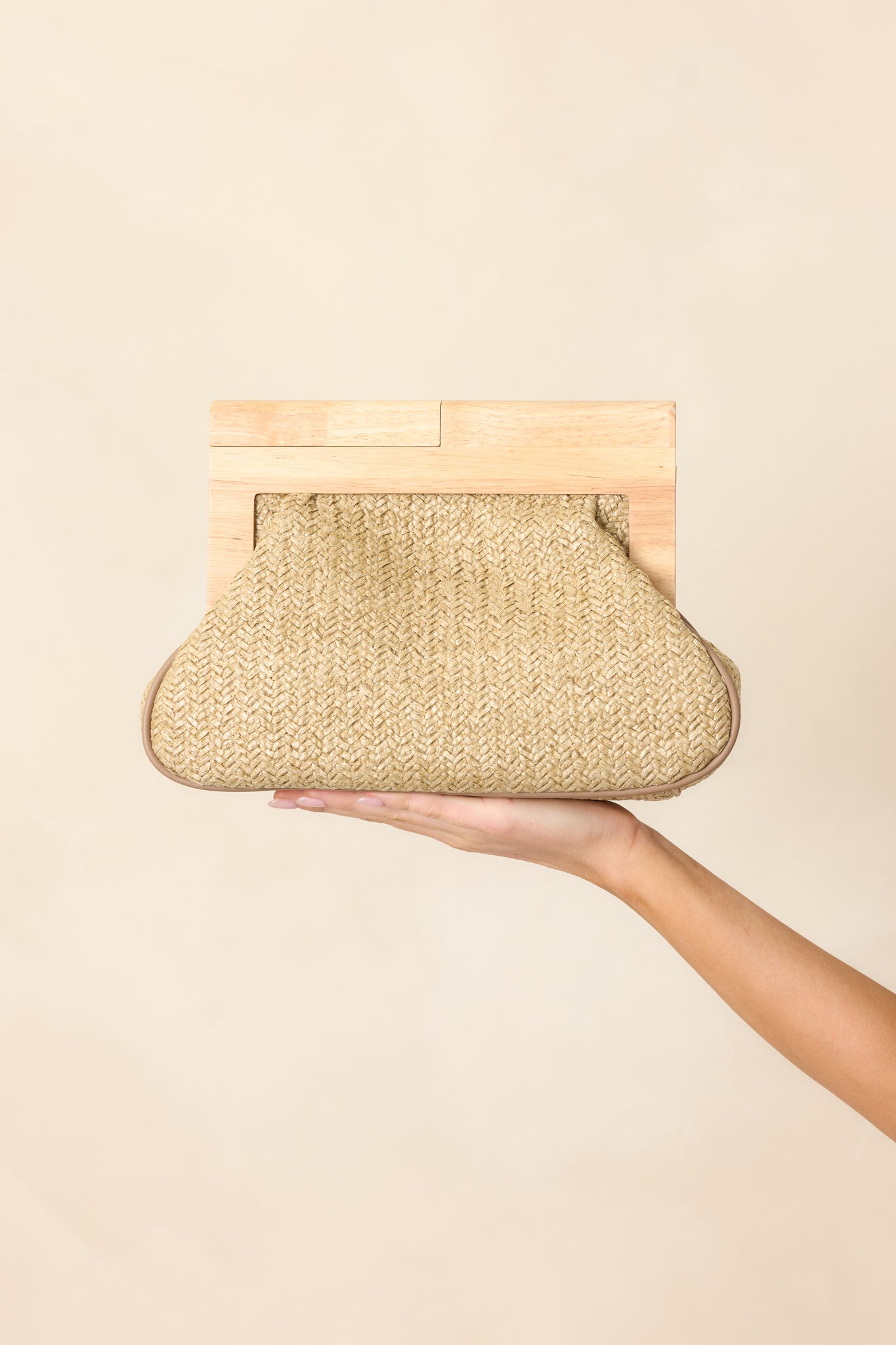 A front-facing view of the natural clutch showcasing its bamboo handle, magnetic closure, and neutral tone