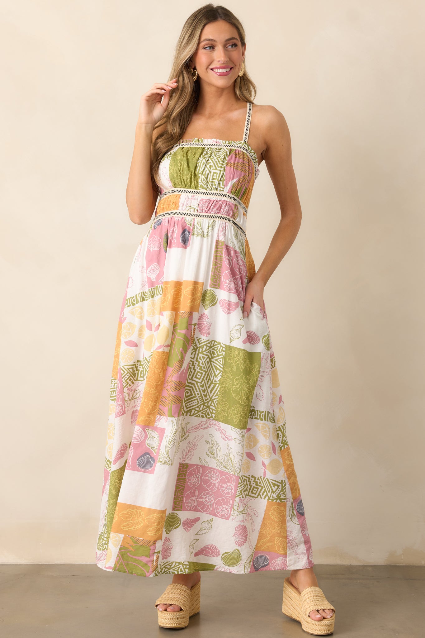 The ivory dress from the front, highlighting its embroidered top detailing, straight neckline with ruffles, and maxi-length skirt with a tropical patchwork print.