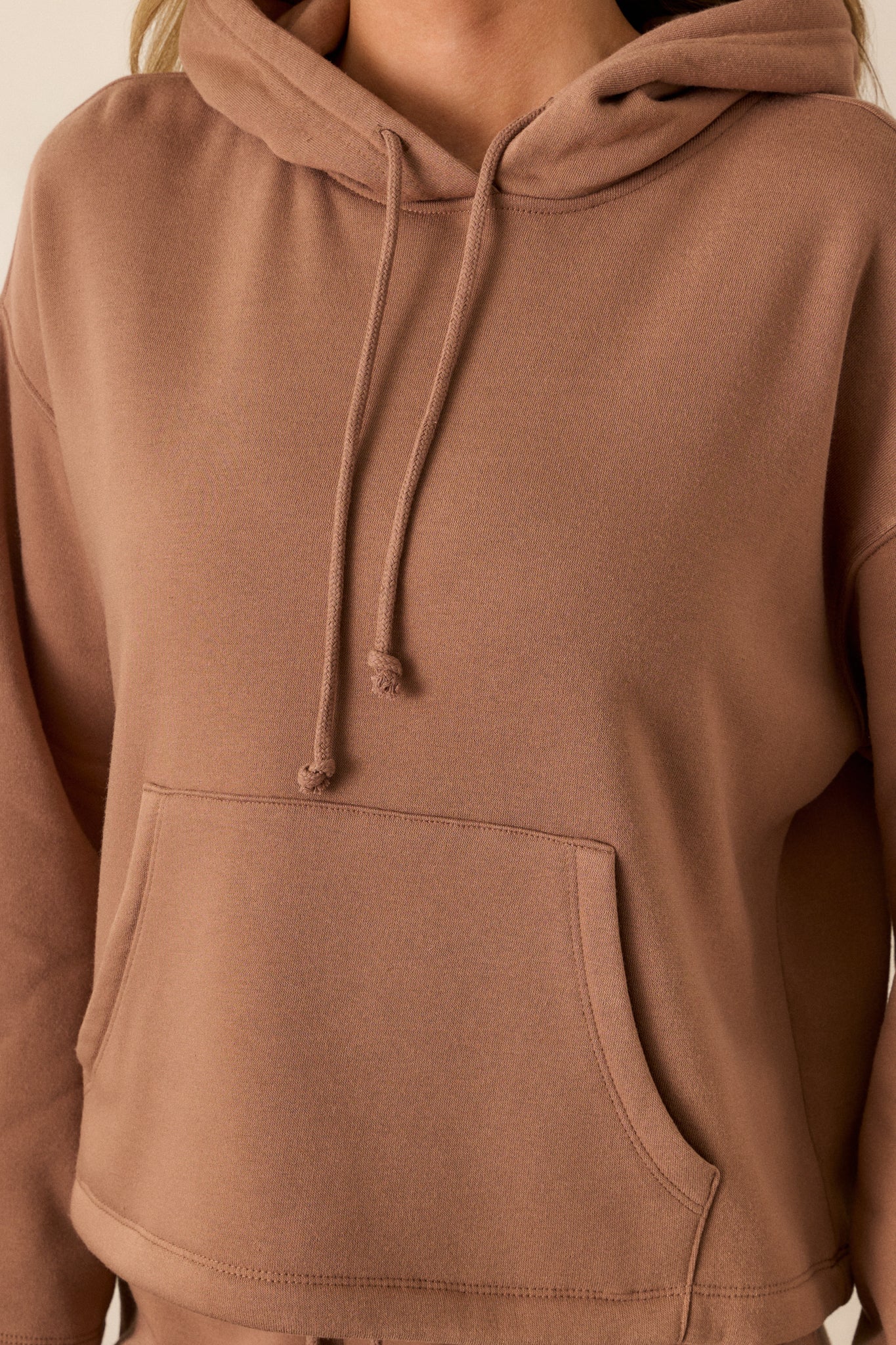 Close-up of the brown sweatshirt’s fabric texture, focusing on the adjustable drawstring and stitching around the kangaroo pocket.