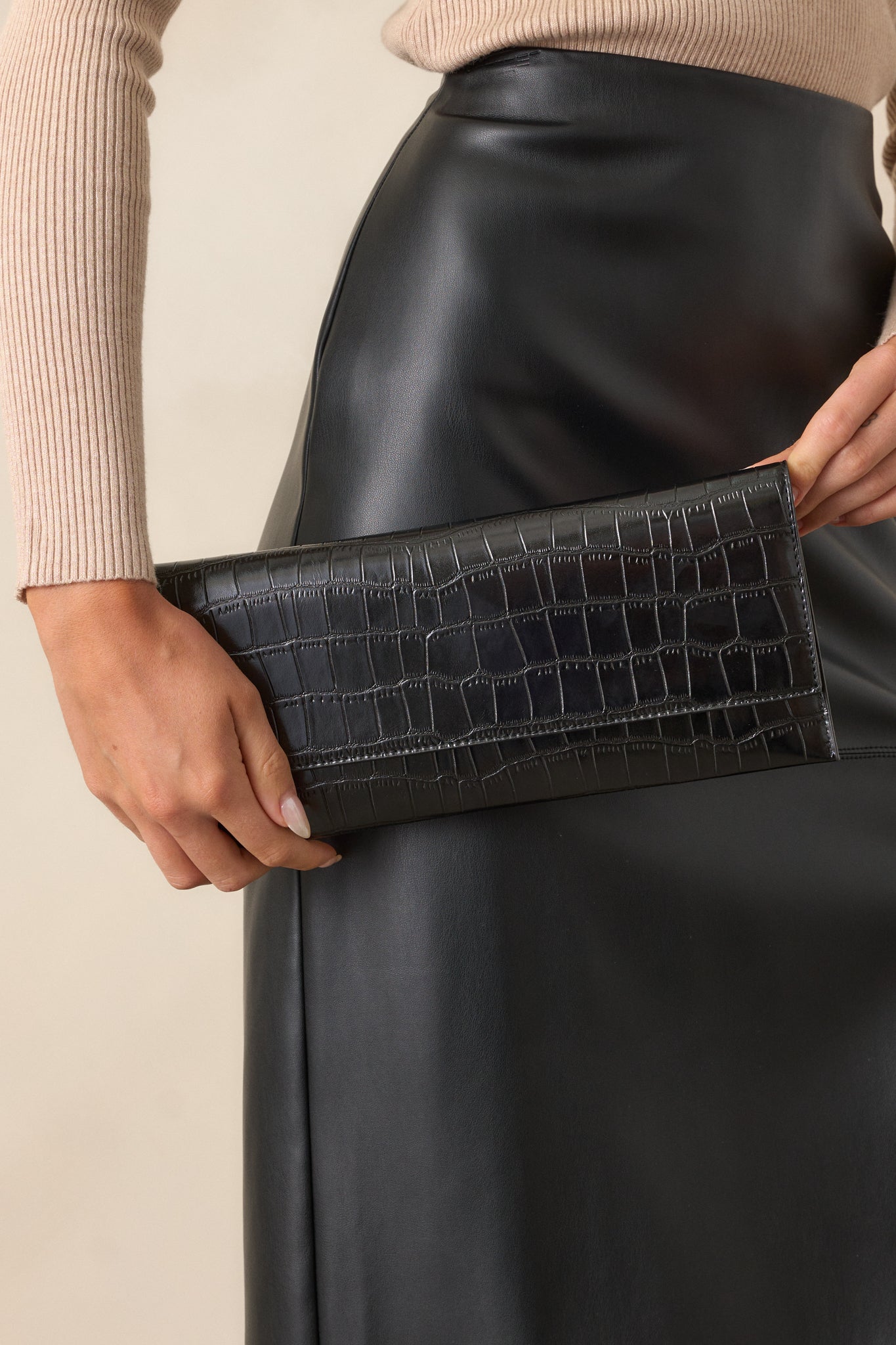 A front view of the black clutch, showcasing its rectangular shape, textured faux leather material, and magnetic fold-over closure.