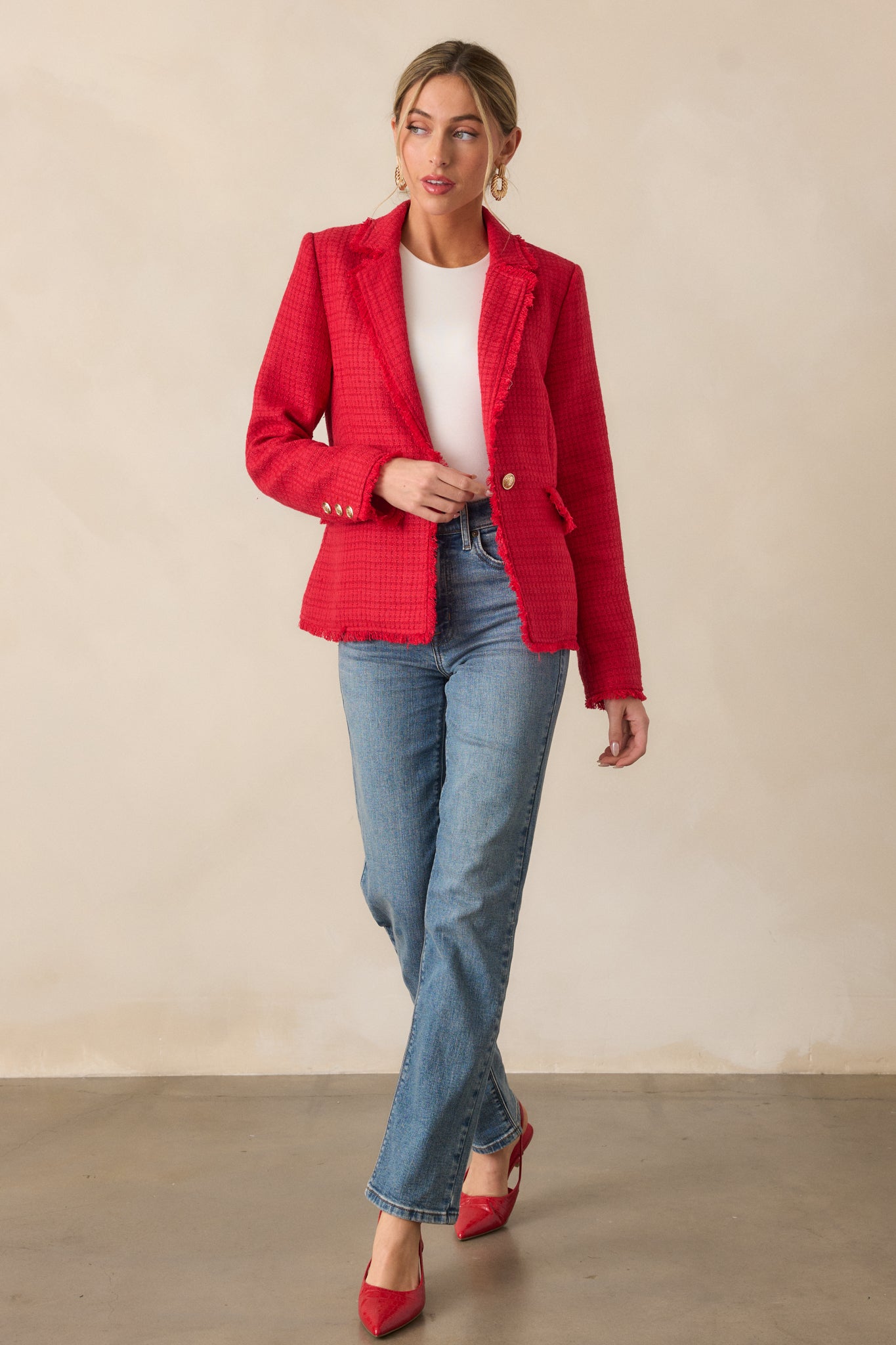 A full-length view of the red blazer, showcasing the lapel collar neckline, long sleeves, and tweed fabric with raw fringe hems.