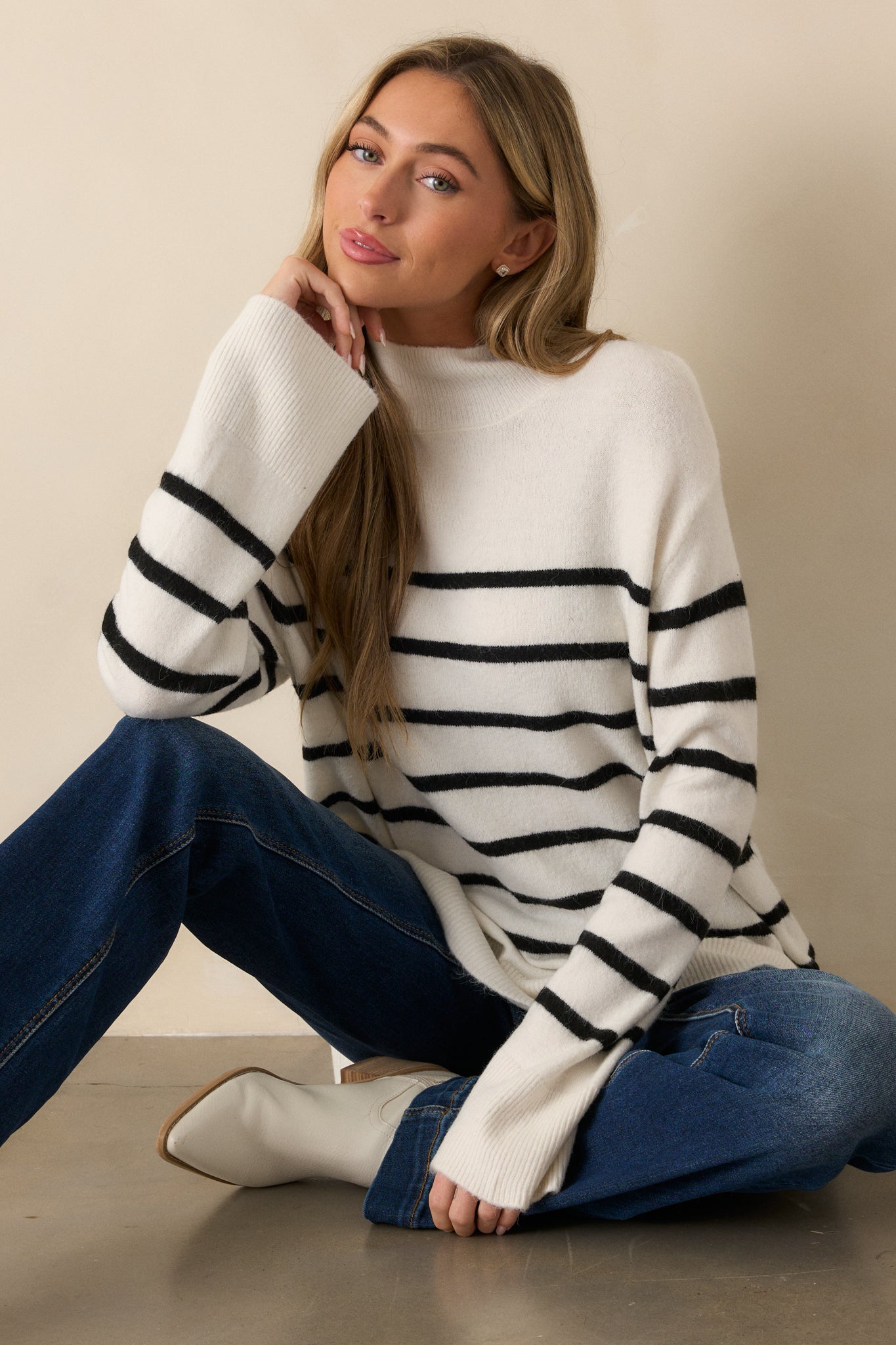 Full-body view of an ivory sweater with a high mock turtle neckline and long bell sleeves, featuring subtle stripe detailing and rib knit hems.