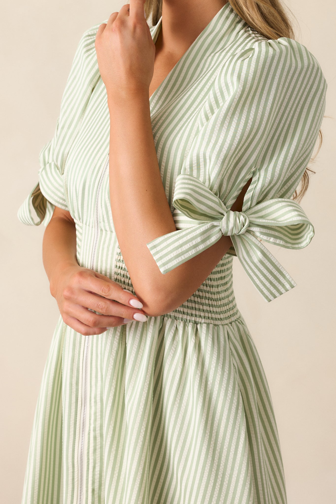 Close-up of the green stripe dress’s smocking detail at the waist, showing the front zipper, V-neck neckline, and part of the striped fabric pattern.