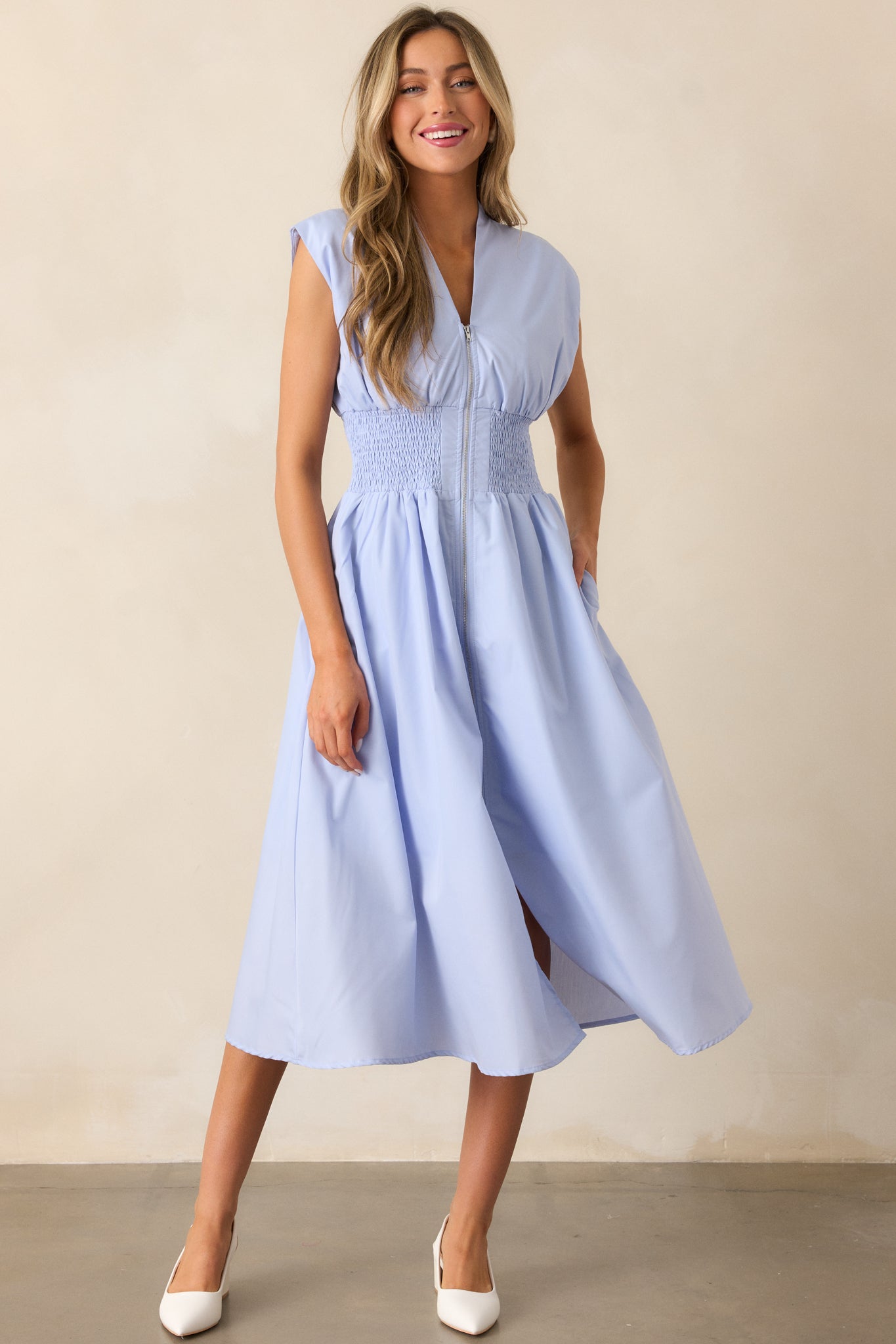 This baby blue midi dress features a chic v-neckline, capped sleeves, a front slit, and functional hip pockets, all highlighted by its comfortable smocked waist.