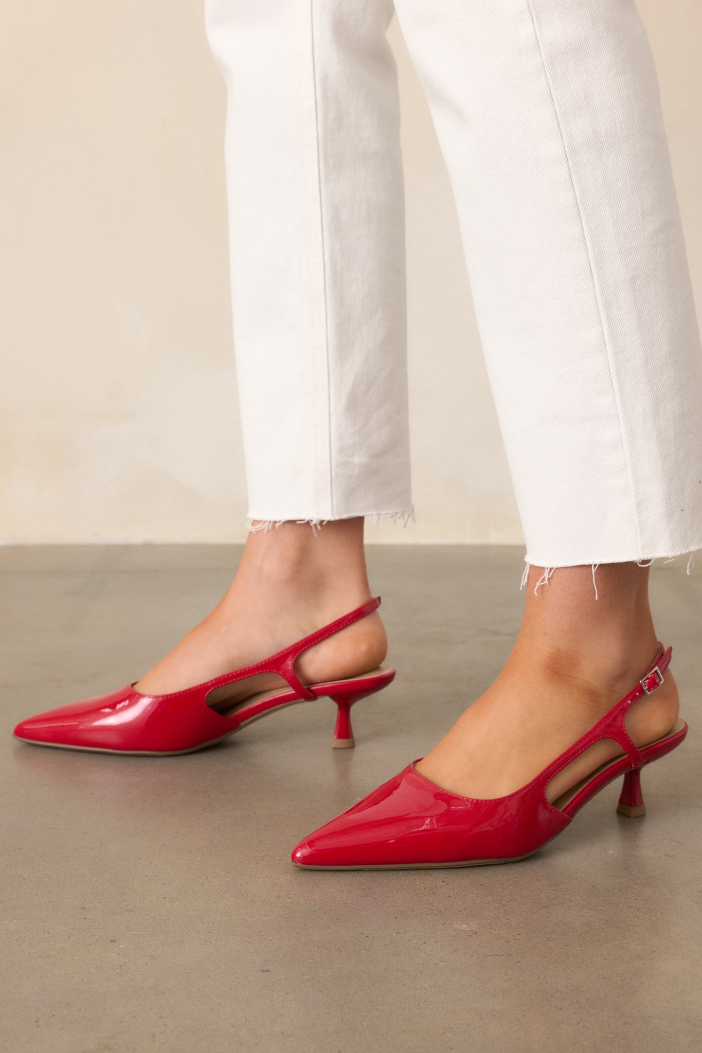 A detailed view of the red heels highlighting the small gold buckle, sleek pointed heel, and subtle cutout design on the side.