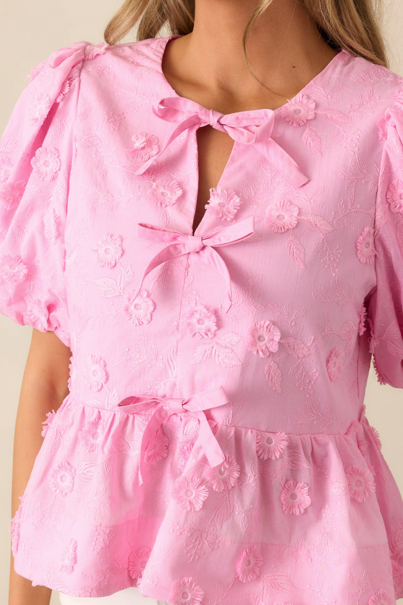 A close-up of the bow front detail and puff sleeves of the pink blouse, highlighting the round neckline and the subtle texture of the fabric.