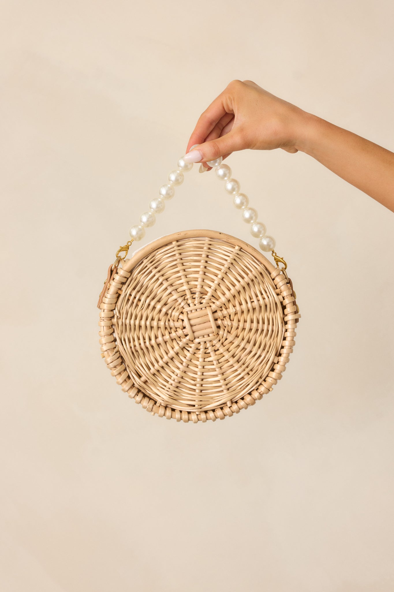 This handbag features a circular shape with two removable faux pearl straps, gold hardware, and a drawstring closure, offering a chic and versatile design.