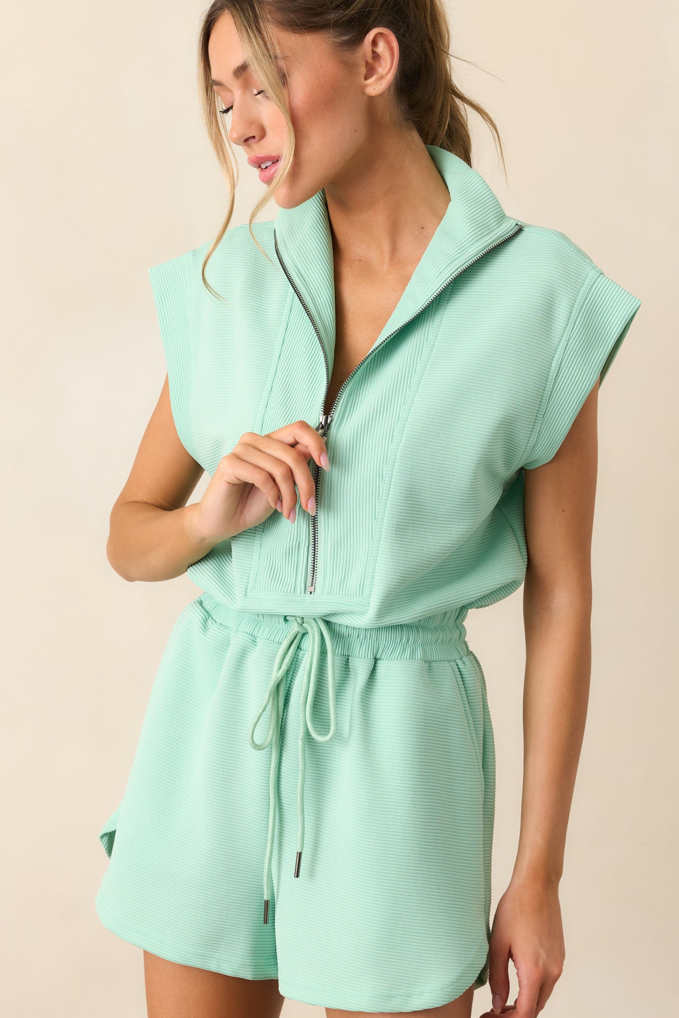 A cropped view of the romper's waist area, highlighting the elastic waistband, self-tie drawstring, and functional hip pockets.