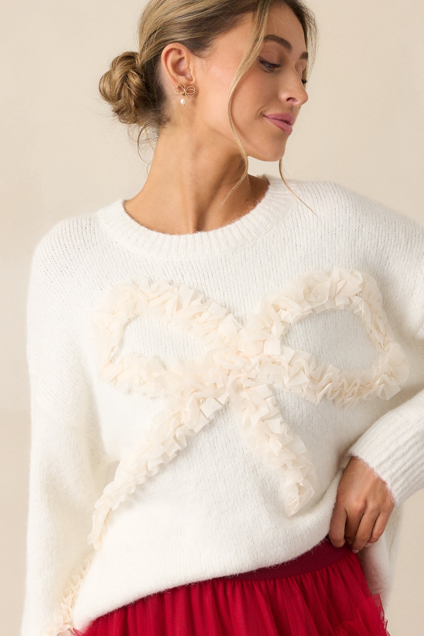 Close-up of the upper portion of the sweater, emphasizing the large ruffle bow detail with pearl accents and the rounded neckline.