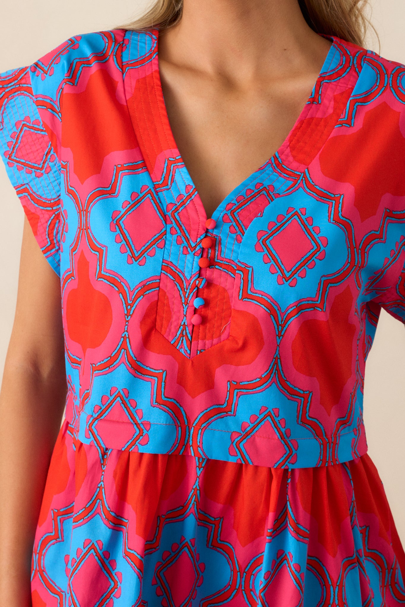 Close-up of the pink and blue print on the red dress, highlighting the vibrant colors and the fine stitching along the flutter sleeves.