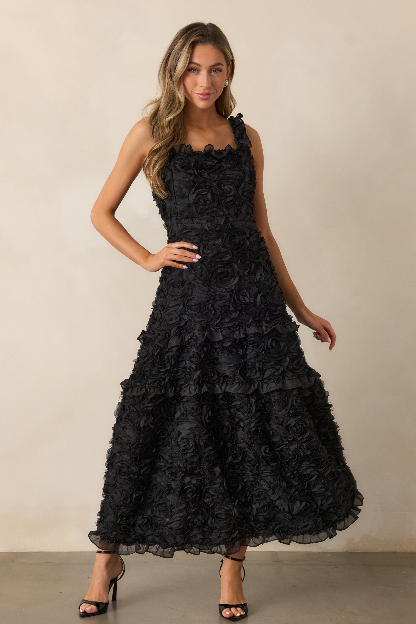 A complete view of the black dress, highlighting the floral appliques and the soft ruffle hem detailing along the skirt.