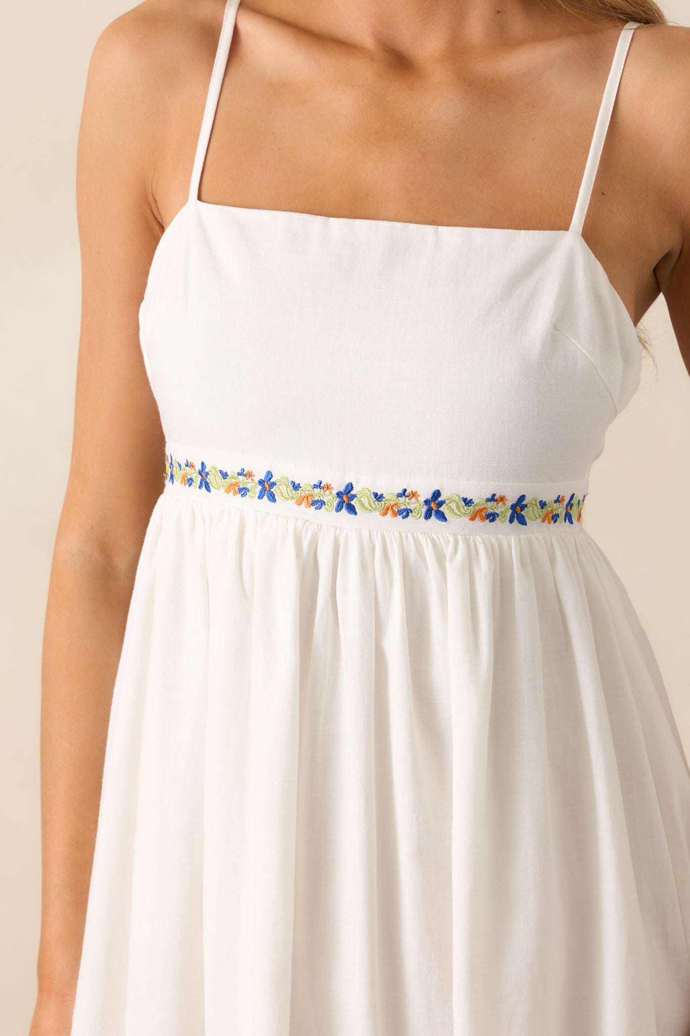 An up-close detail shot of the ivory dress’s floral embroidered detailing and smooth fabric under the bust.