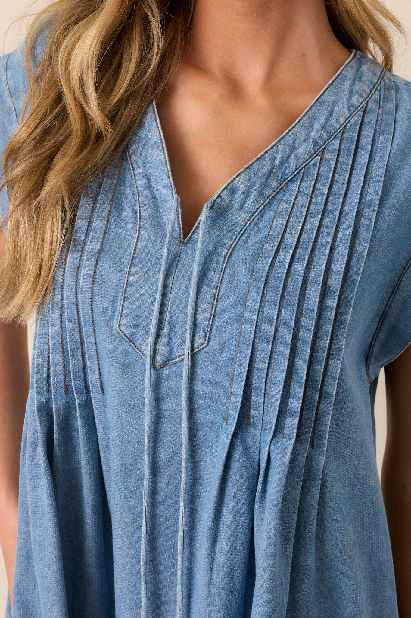 Close-up of this chambray dress that features a v-neckline, a self-tie feature, functional pockets, and pin tuck pleating around neckline.