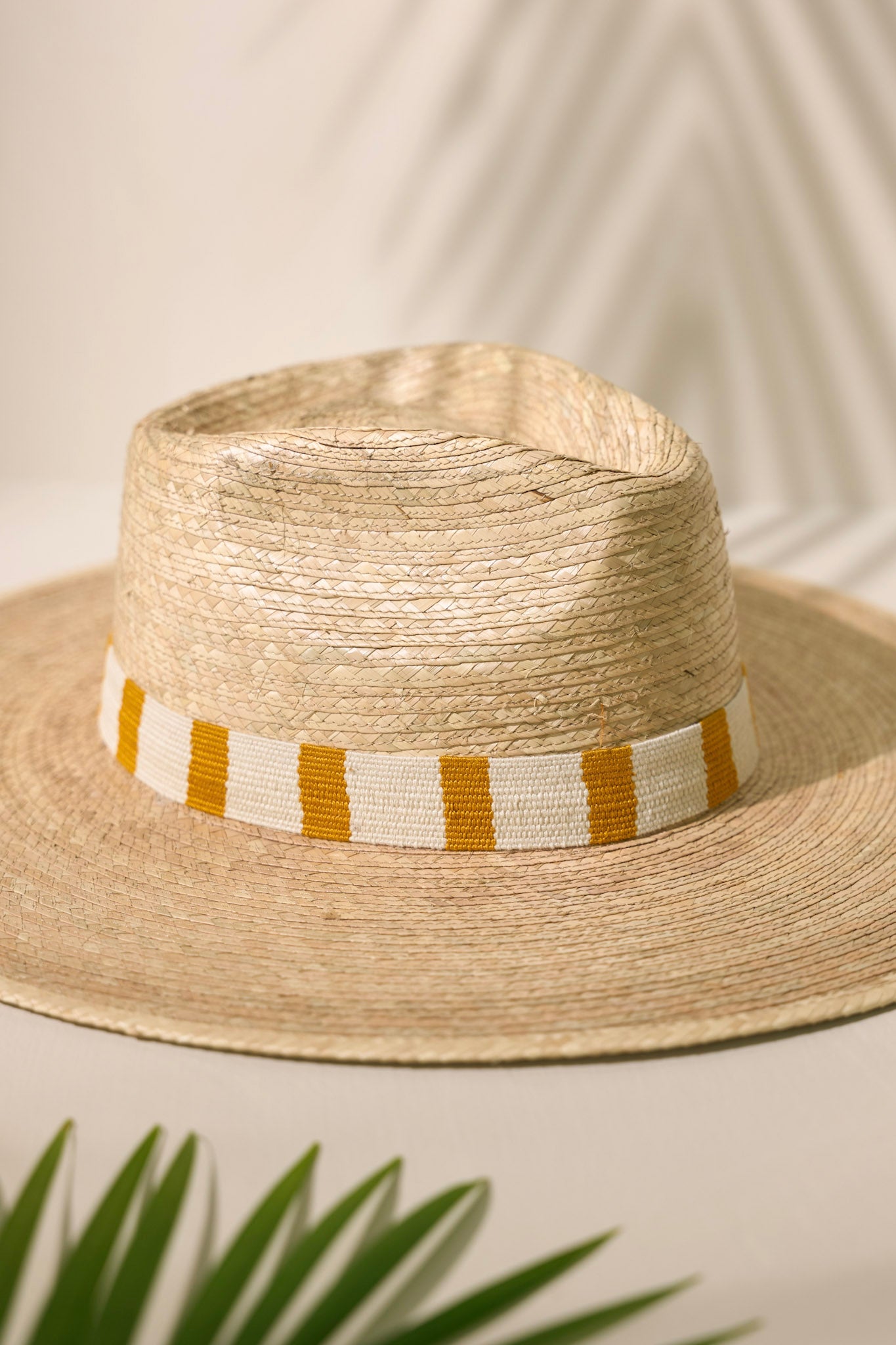 Close-up view of this Carmen Palm Hat features a cotton woven band with mustard yellow and white stripes, and is handmade with palm fronds.