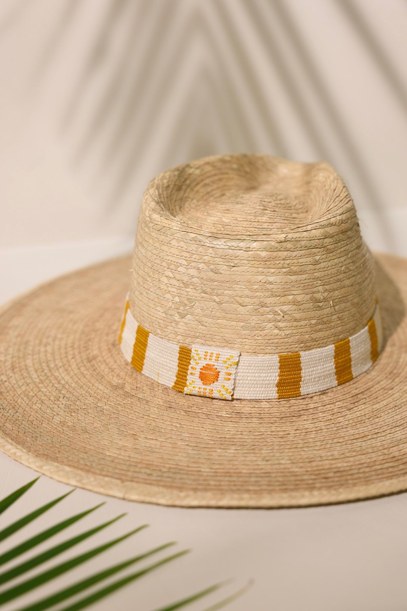 Front close-up view of this Carmen Palm Hat features a cotton woven band with mustard yellow and white stripes, and is handmade with palm fronds.